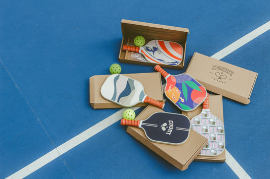 Image of 4 Court Pickleball Paddles layed out on their boxes on a pickleball court. 